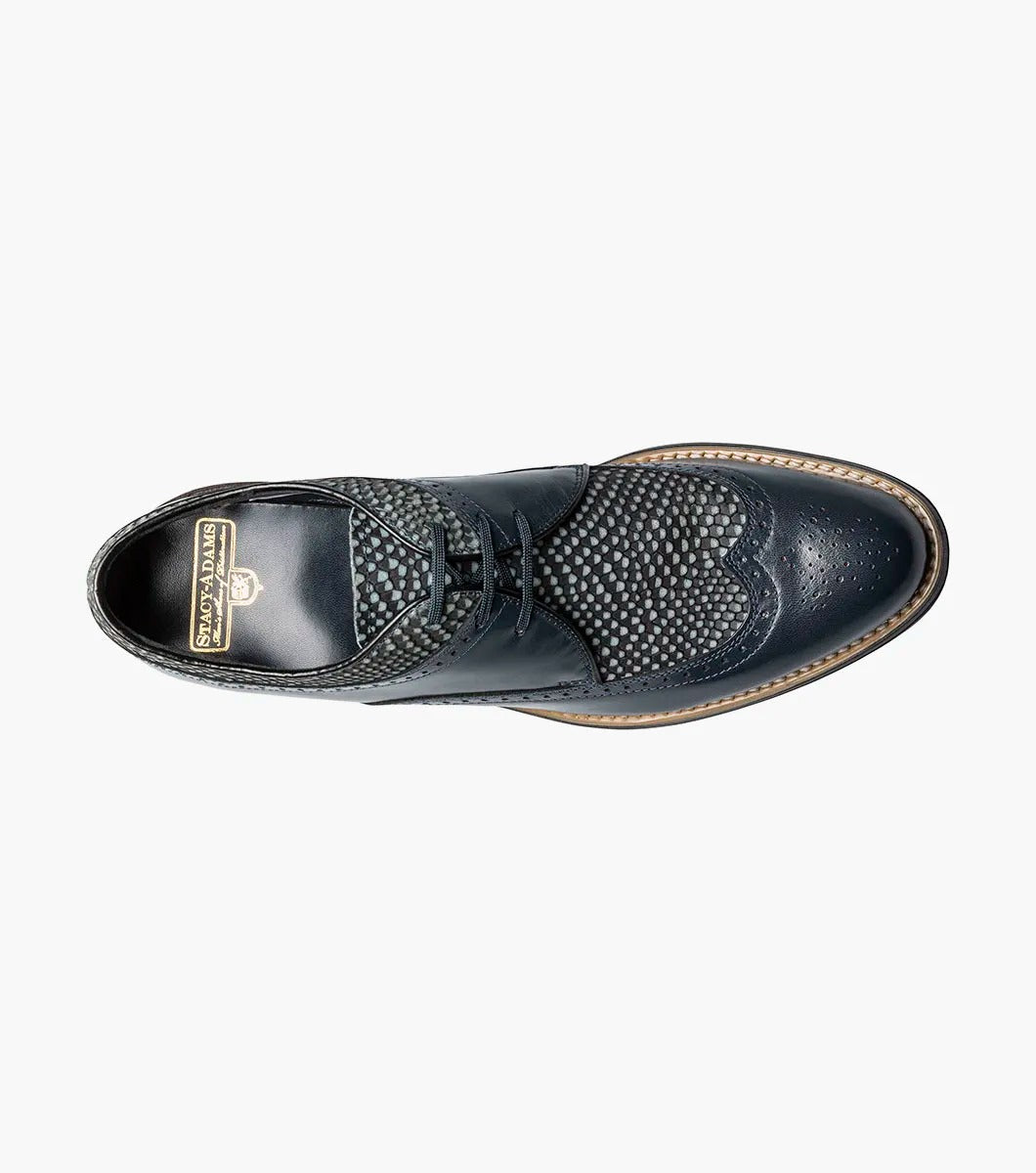 The Stacy Adams DAYTON Python Print Wingtip Oxford in navy is a sophisticated shoe, showcasing textured paneling and made from Kidskin leather. It includes sleek black laces and a polished wooden sole.