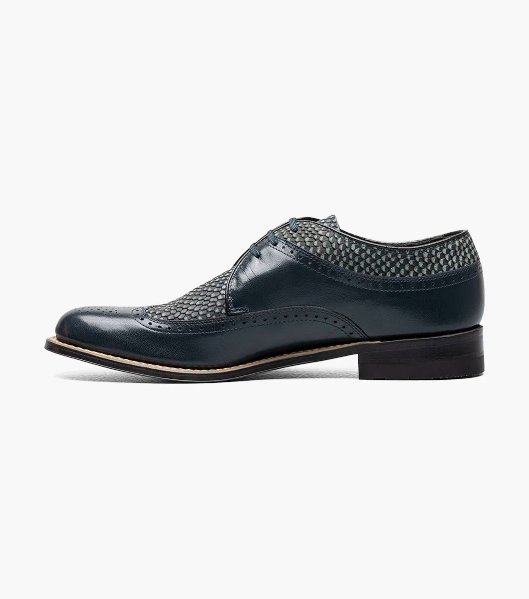 The Stacy Adams DAYTON Python Print Wingtip Oxford in navy is a sophisticated shoe, showcasing textured paneling and made from Kidskin leather. It includes sleek black laces and a polished wooden sole.