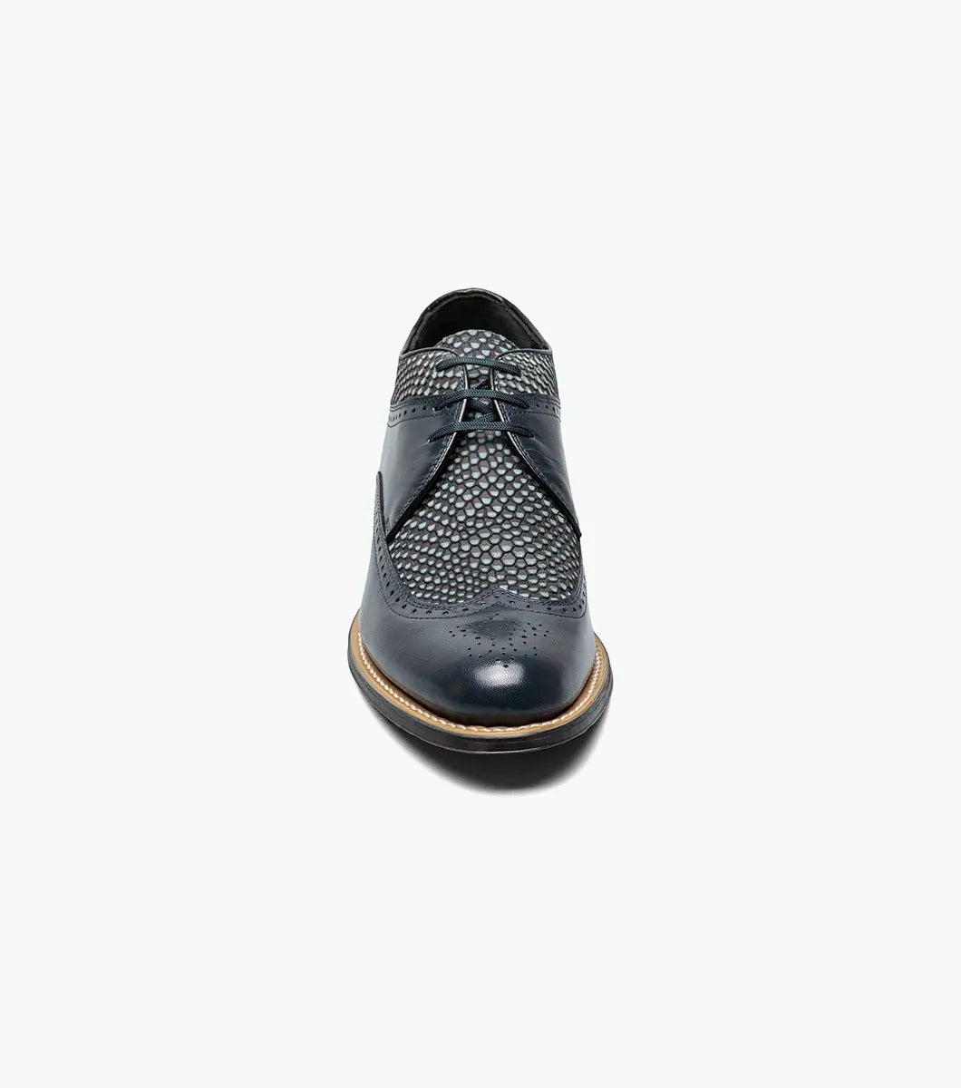 The Stacy Adams DAYTON Python Print Wingtip Oxford in navy is a sophisticated shoe, showcasing textured paneling and made from Kidskin leather. It includes sleek black laces and a polished wooden sole.