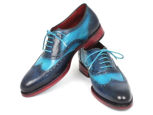 The Paul Parkman Two Tone Wingtip Oxfords in Blue & Turquoise (27TQ88) display an exquisite finish with hand-painted leather details, featuring teal accents and striking red soles, all set against a plain backdrop.