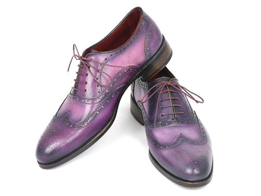 Two exquisite pairs of Paul Parkman Wingtip Oxfords in a blend of purple and navy, crafted from hand-painted calfskin leather with decorative perforations and maroon laces, are artfully crossed over each other on a white background.
