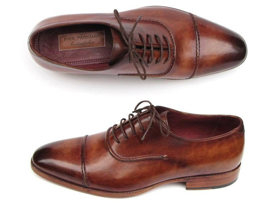 The Paul Parkman Captoe Oxfords Brown Hand Painted Shoes (model 077-BRW) highlight exquisite craftsmanship in a pair of Oxford captoe style brown leather dress shoes with laces, viewed from the top and side. These handcrafted shoes feature a sleek leather upper, embodying timeless elegance for any formal occasion.
