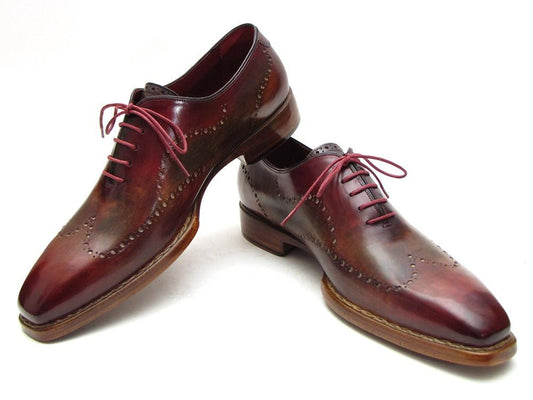 The Paul Parkman Wingtip Oxford Goodyear Welted Bordeaux & Camel - 087LX, featuring polished brown leather and red laces with brogue detailing, showcases their exquisite craftsmanship as handmade leather Oxfords against a plain background.