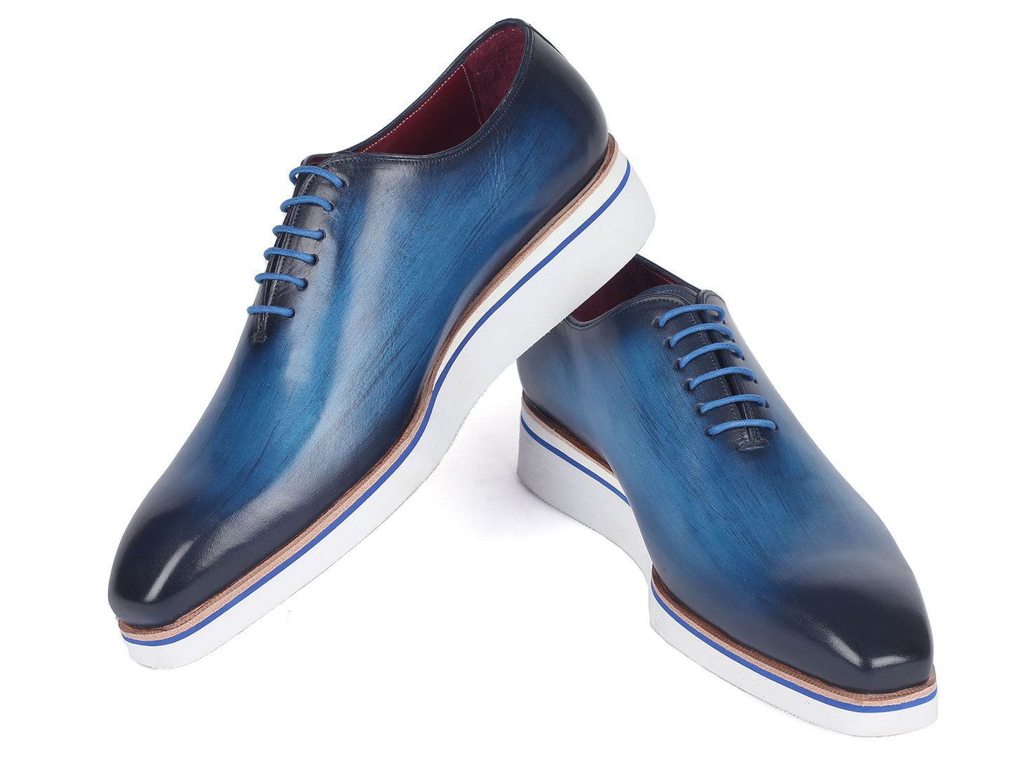 A pair of Paul Parkman Men's Smart Casual Wholecut Oxfords in vibrant blue, featuring distinctive white soles and matching blue laces, meticulously crafted from hand-painted leather, showcased against a plain backdrop.