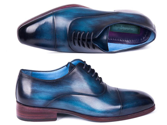 A pair of Paul Parkman Captoe Oxfords Blue & Turquoise - 1744-BTQ, expertly crafted from hand-painted leather, is showcased. One shoe stands upright to display its side, while the other is positioned on its side to reveal the Paul Parkman brand label inside.