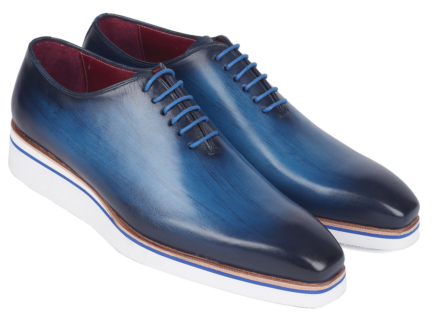 A pair of Paul Parkman Men's Smart Casual Wholecut Oxfords in vibrant blue, featuring distinctive white soles and matching blue laces, meticulously crafted from hand-painted leather, showcased against a plain backdrop.