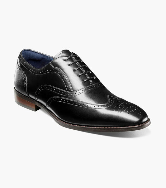 The Stacy Adams Kaine Wingtip Oxford (25569-001) is a black leather dress shoe with brogue detailing, anatomical arch support, and a low wooden heel by STACY ADAMS, shown on a white background.