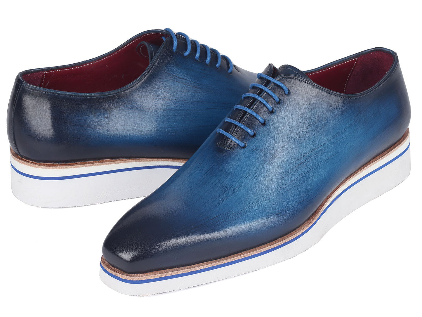 A pair of Paul Parkman Men's Smart Casual Wholecut Oxfords in vibrant blue, featuring distinctive white soles and matching blue laces, meticulously crafted from hand-painted leather, showcased against a plain backdrop.