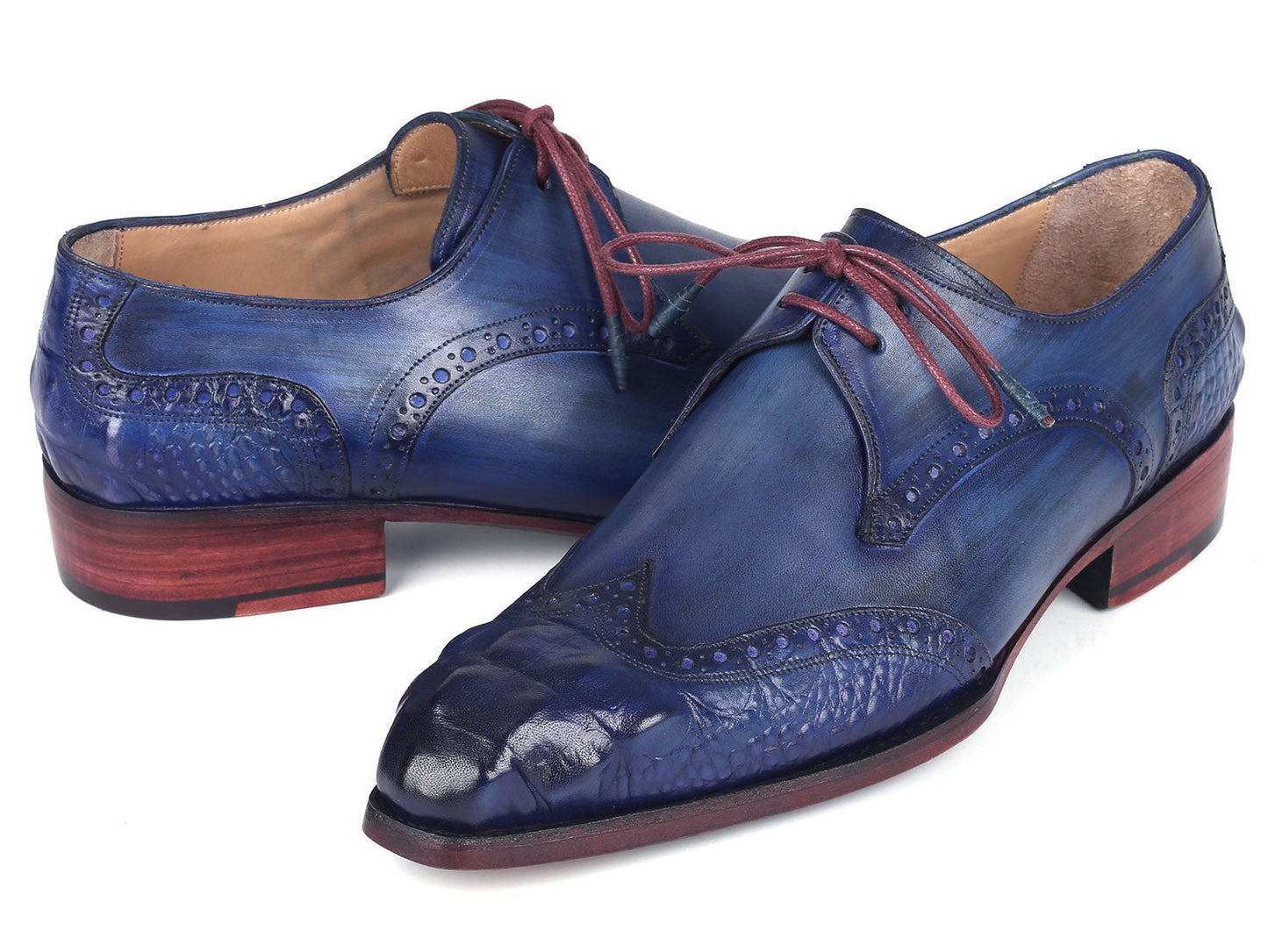 The Paul Parkman Goodyear Welted Wingtip Derby Shoes Blue & Navy - 584-BLU showcase a stunning design in blue leather with intricate detailing and vibrant red laces. Displayed beautifully, one shoe is elegantly laid on its side while the other stands upright. These meticulously handmade shoes feature the renowned Goodyear welted craftsmanship, ensuring both elegance and durability.