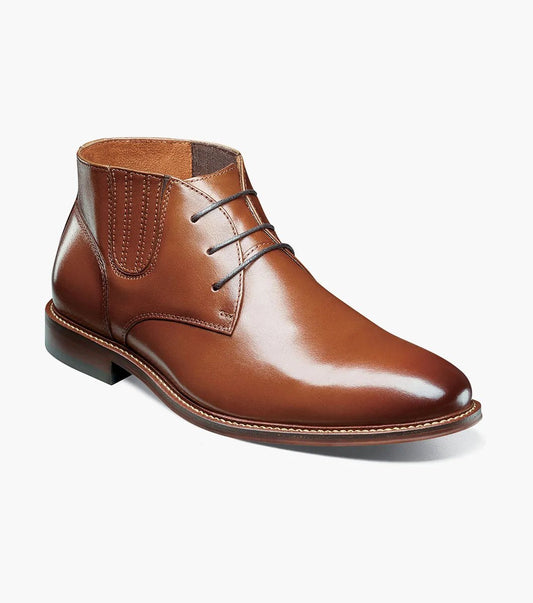 The STACY ADAMS Maxwell Plain Toe Chukka Boot in cognac (25551-221) features closed lacing, a stitched welt, and low heel, shown against a white background.