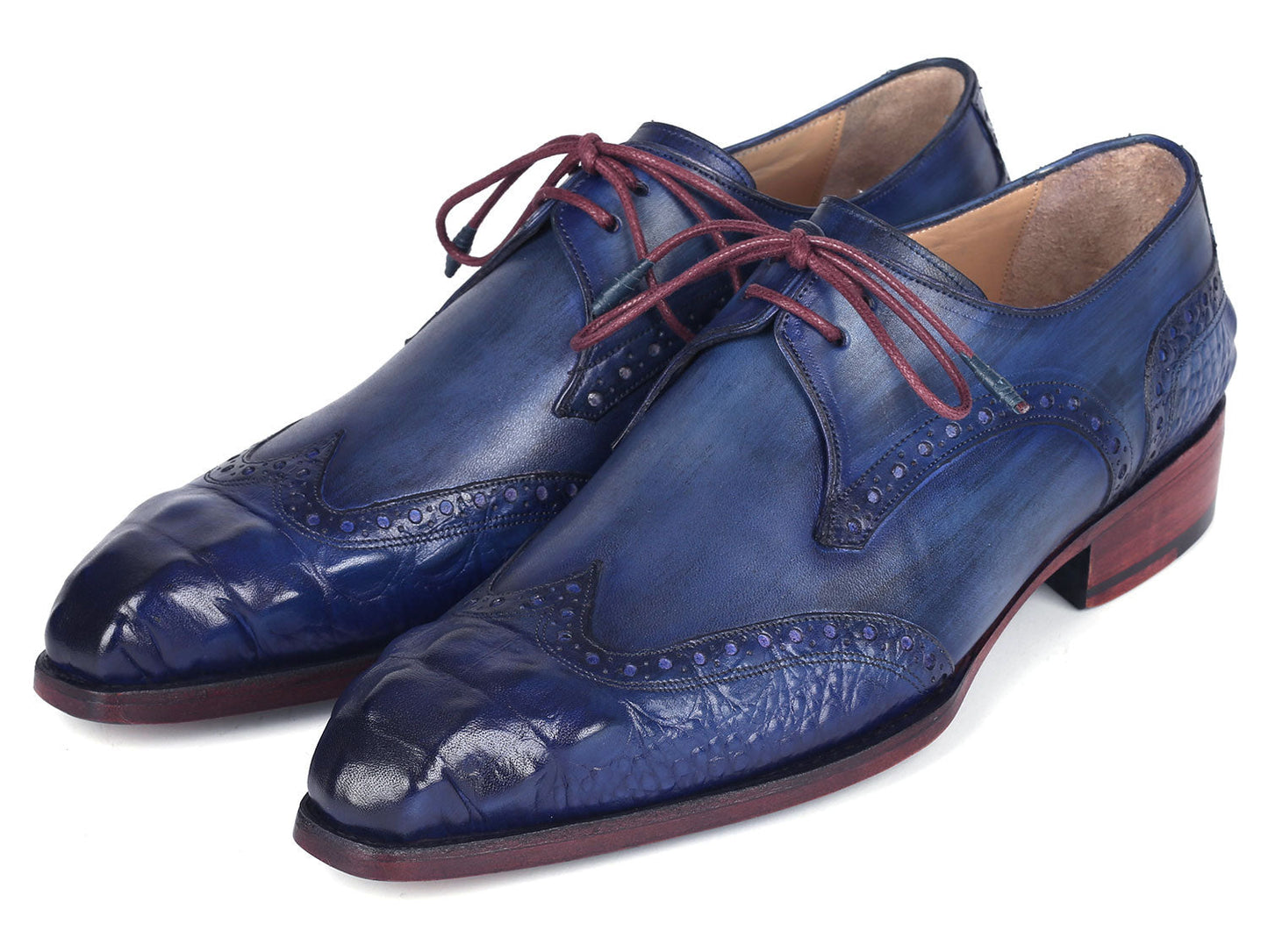 The Paul Parkman Goodyear Welted Wingtip Derby Shoes Blue & Navy - 584-BLU showcase a stunning design in blue leather with intricate detailing and vibrant red laces. Displayed beautifully, one shoe is elegantly laid on its side while the other stands upright. These meticulously handmade shoes feature the renowned Goodyear welted craftsmanship, ensuring both elegance and durability.