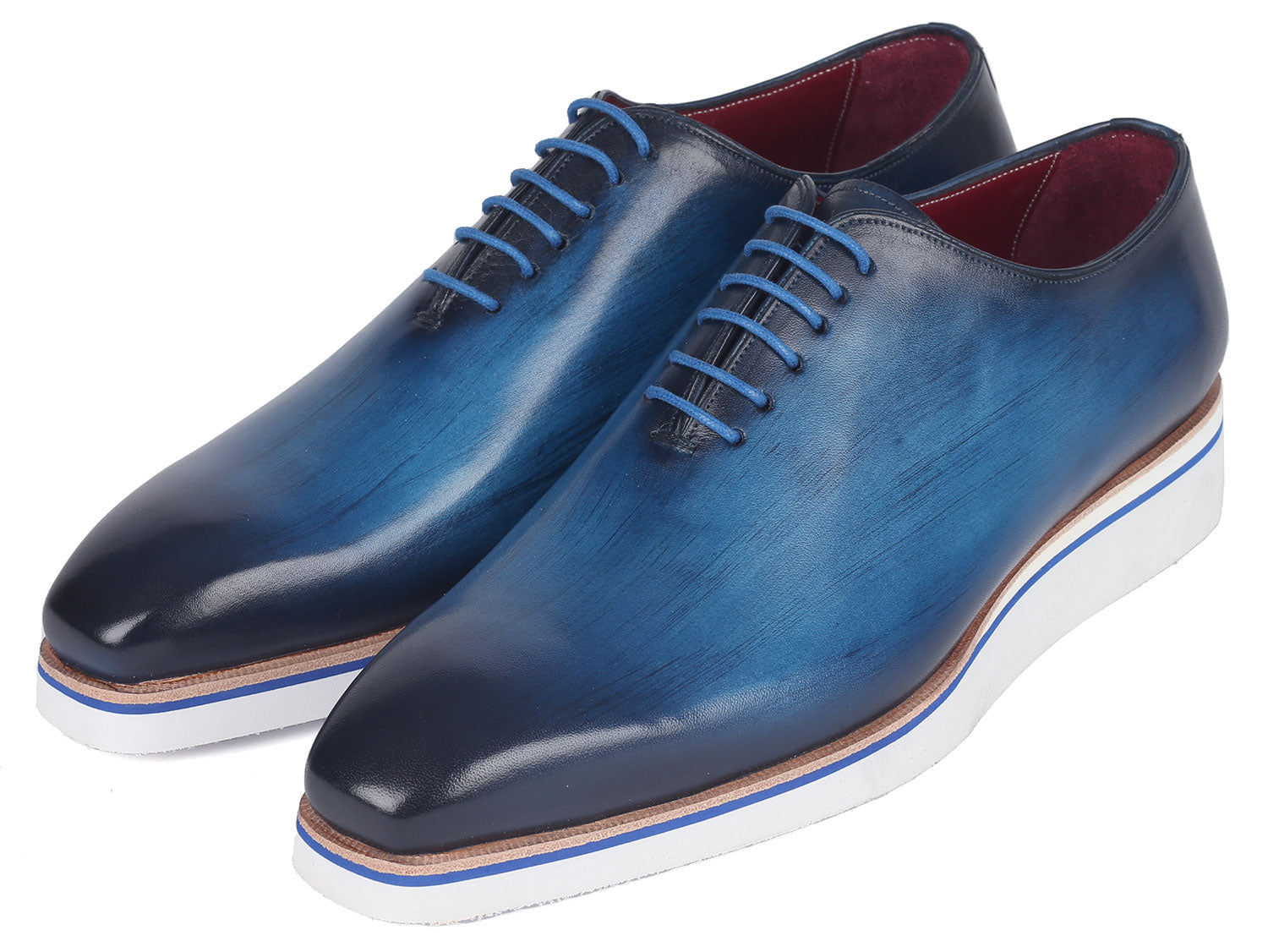 A pair of Paul Parkman Men's Smart Casual Wholecut Oxfords in vibrant blue, featuring distinctive white soles and matching blue laces, meticulously crafted from hand-painted leather, showcased against a plain backdrop.