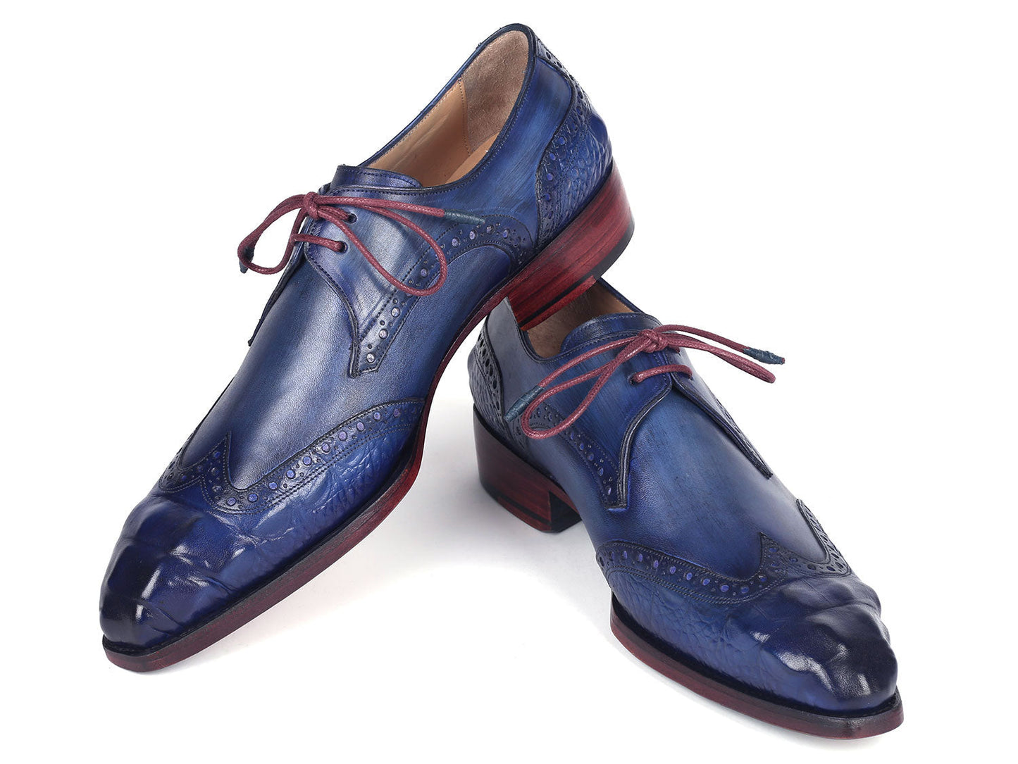 The Paul Parkman Goodyear Welted Wingtip Derby Shoes Blue & Navy - 584-BLU showcase a stunning design in blue leather with intricate detailing and vibrant red laces. Displayed beautifully, one shoe is elegantly laid on its side while the other stands upright. These meticulously handmade shoes feature the renowned Goodyear welted craftsmanship, ensuring both elegance and durability.