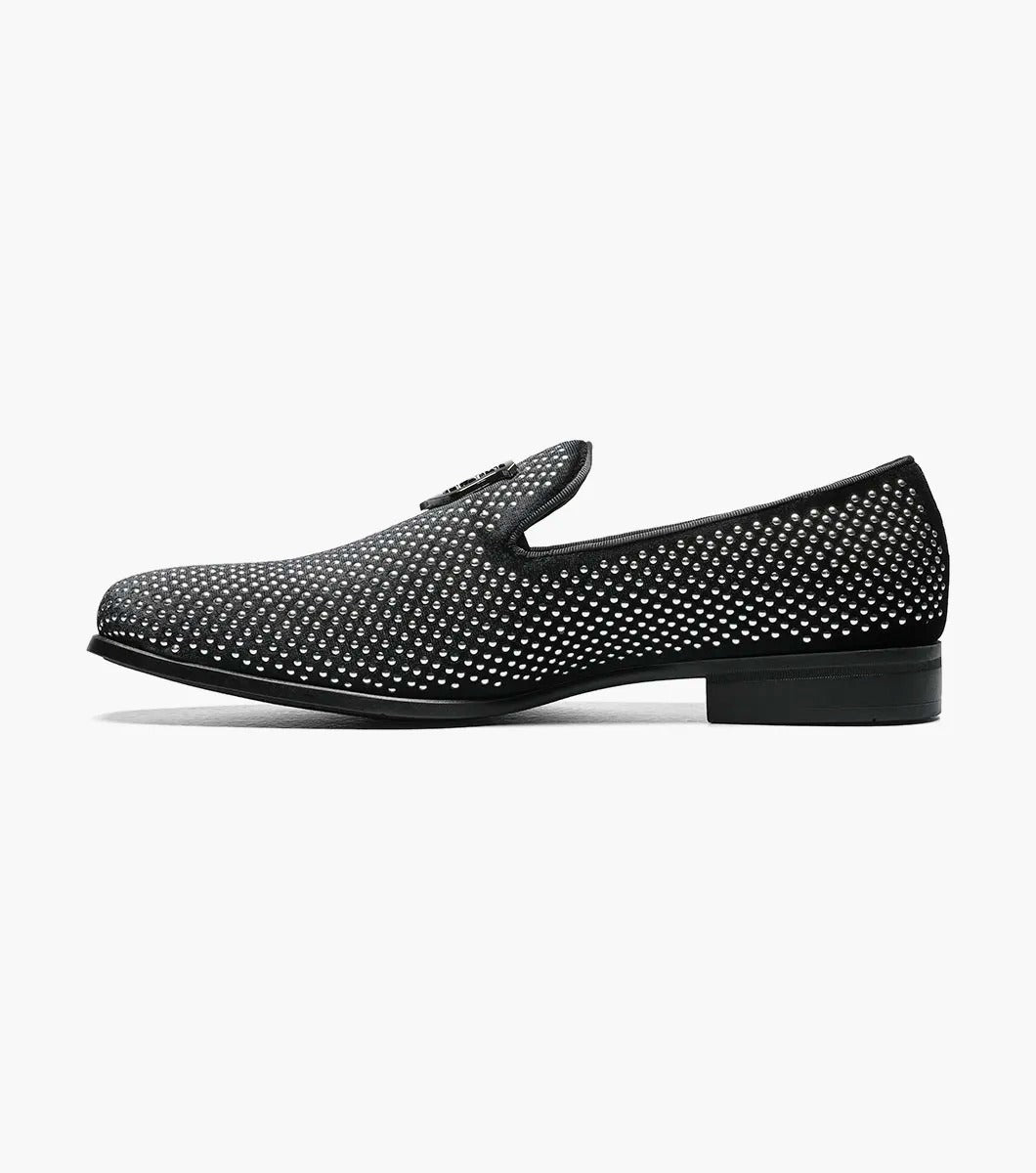 The STACY ADAMS SWAGGER Studded Slip On in black and silver, model 25228-042, is a loafer featuring striking silver studs and the Stacy Adams crest on the upper, exuding a sense of understated elegance.

