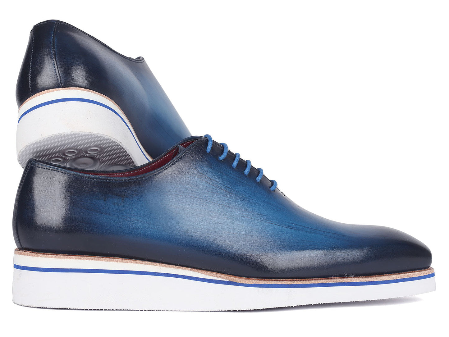 A pair of Paul Parkman Men's Smart Casual Wholecut Oxfords in vibrant blue, featuring distinctive white soles and matching blue laces, meticulously crafted from hand-painted leather, showcased against a plain backdrop.