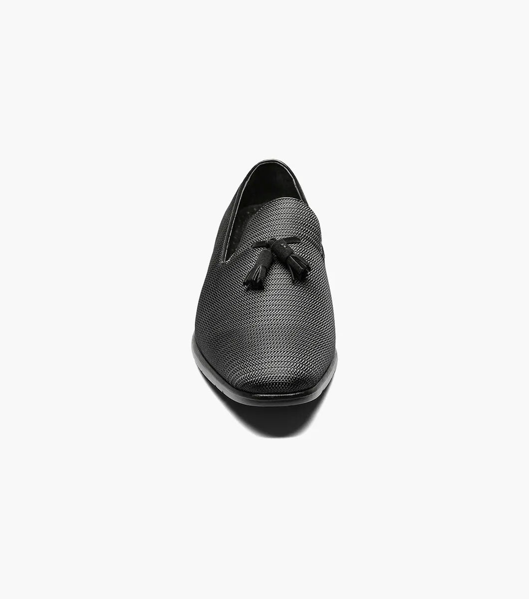 The STACY ADAMS Tazewell Plain Toe Tassel Slip On in black (25343-001) features textured leather, decorative tassels, a low heel, and cushioned footbed, shown on a white background.