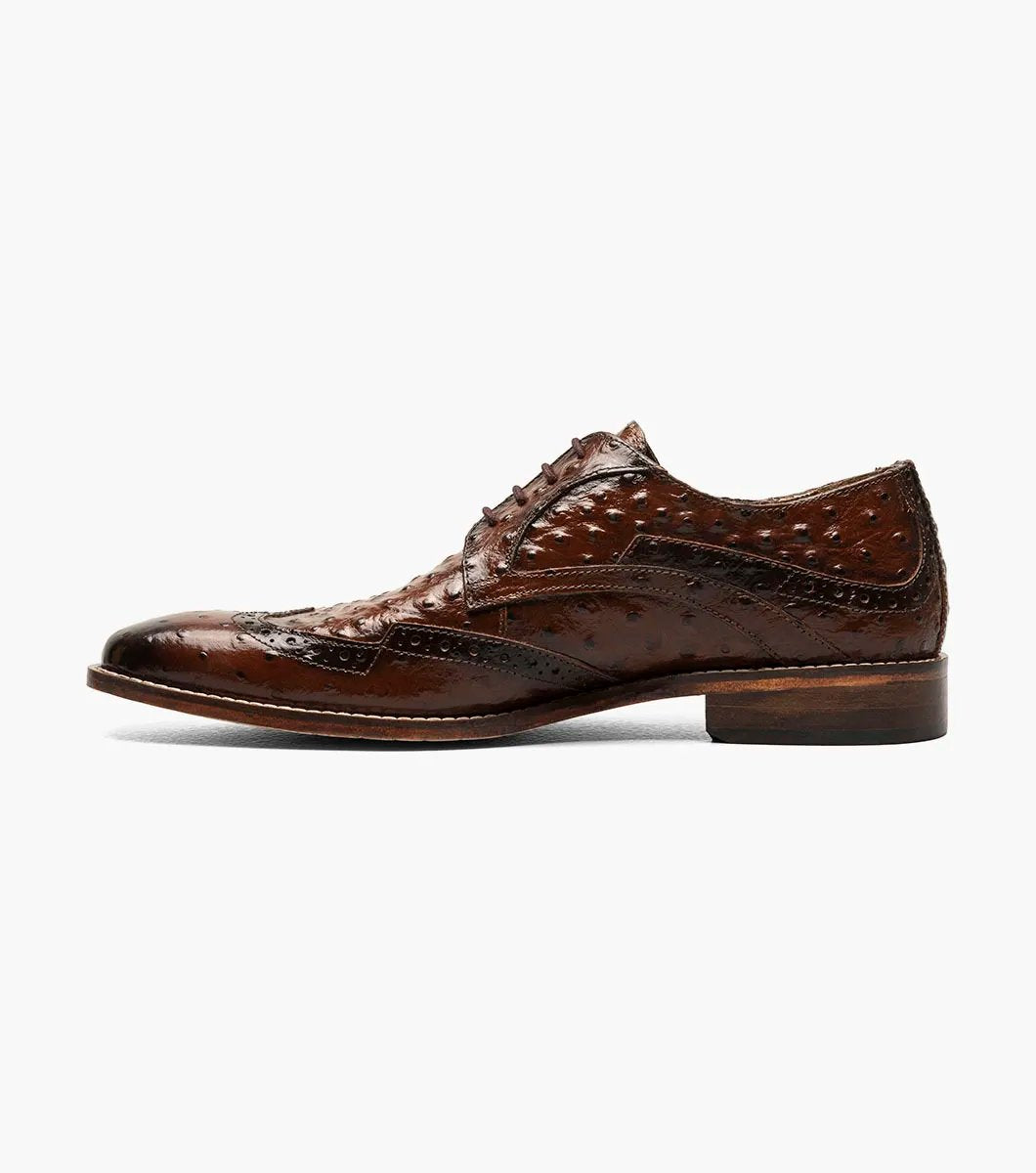 The Stacy Adams GENNARO Wingtip Oxford in cognac showcases a brown ostrich quill print leather design with intricate brogue detailing and a lace-up closure, complemented by anatomical arch support, offering an elegant side view.