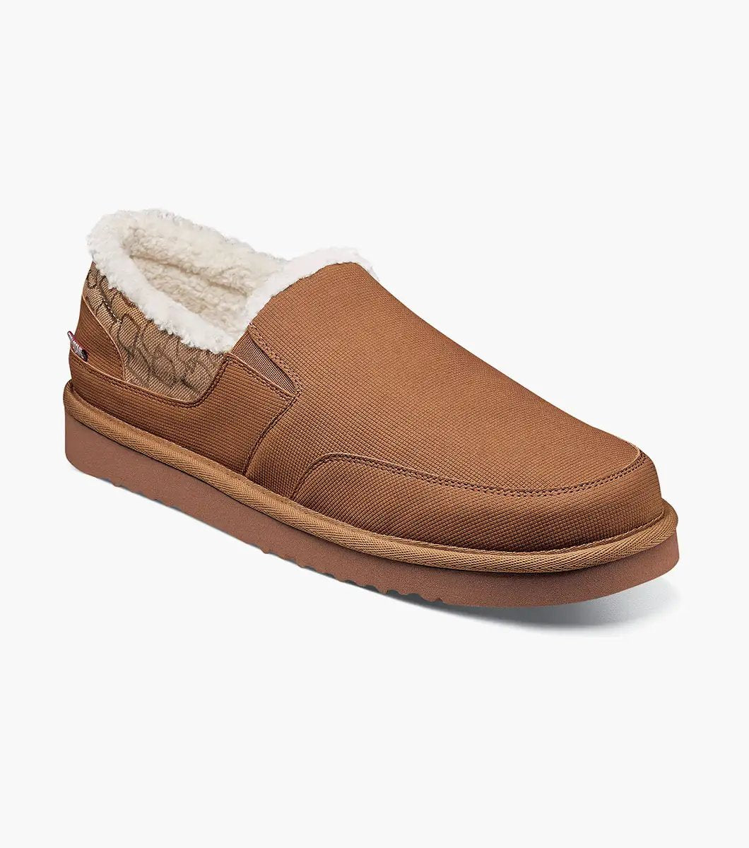 The Stacy Adams Coze Moc Toe Slip On in Tan Multi features a textured upper, plush faux shearling lining, and flat rubber sole, shown on a white background.