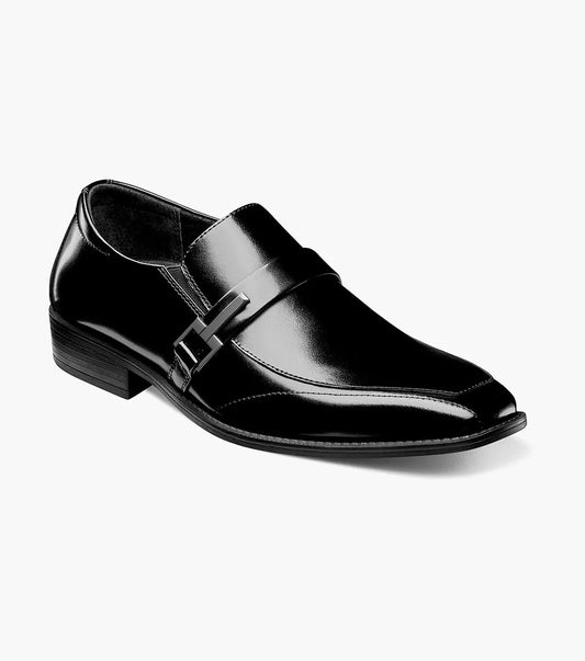 The Stacy Adams Abram Moc Toe Bit Slip On (Black, 20186-001) men's dress shoe features a low heel and metallic buckle detail, shown on a white background.