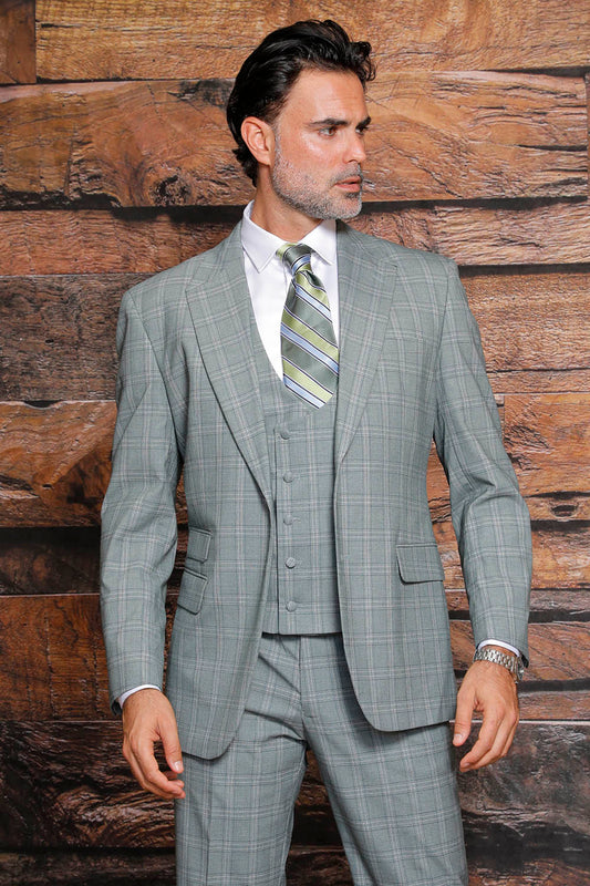 A man wearing the MANZINI Beverly Green Suit by Manzini, featuring a gray plaid design with a modern fit and flat front pants, is complemented by a green striped tie as he stands against a wooden background.