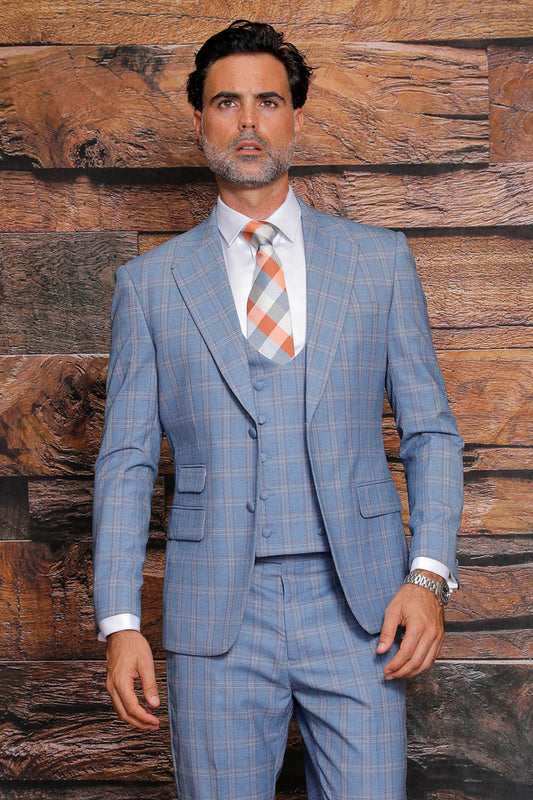 A gentleman in a MANZINI Beverly Sky Suit, featuring a blue plaid pattern and checkered tie, complemented by flat front pants, stands against a wooden backdrop. His Modern Fit attire from Manzini, complete with side vents, radiates effortless style and sophistication.