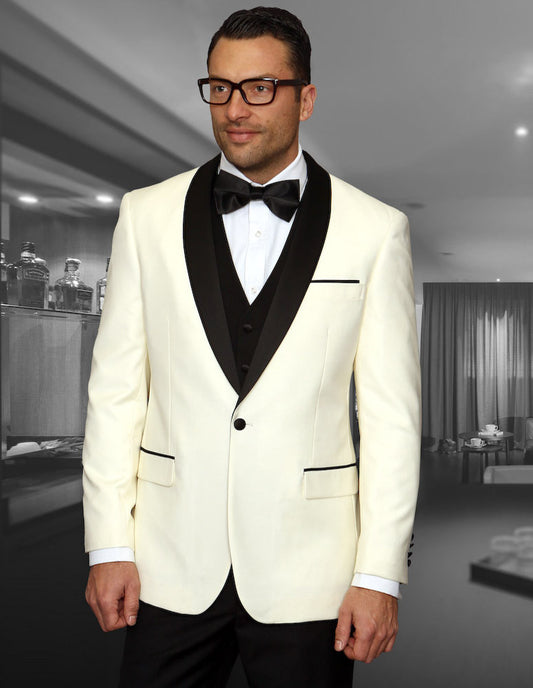 A man dressed in the STATEMENT CLOTHING | ENCORE-OFFWHT tuxedo by Statement Clothing, featuring a white jacket with a black lapel and matching bow tie, is standing in a room with a bar and elegant decor, highlighting the tailored fit and flat front pants.