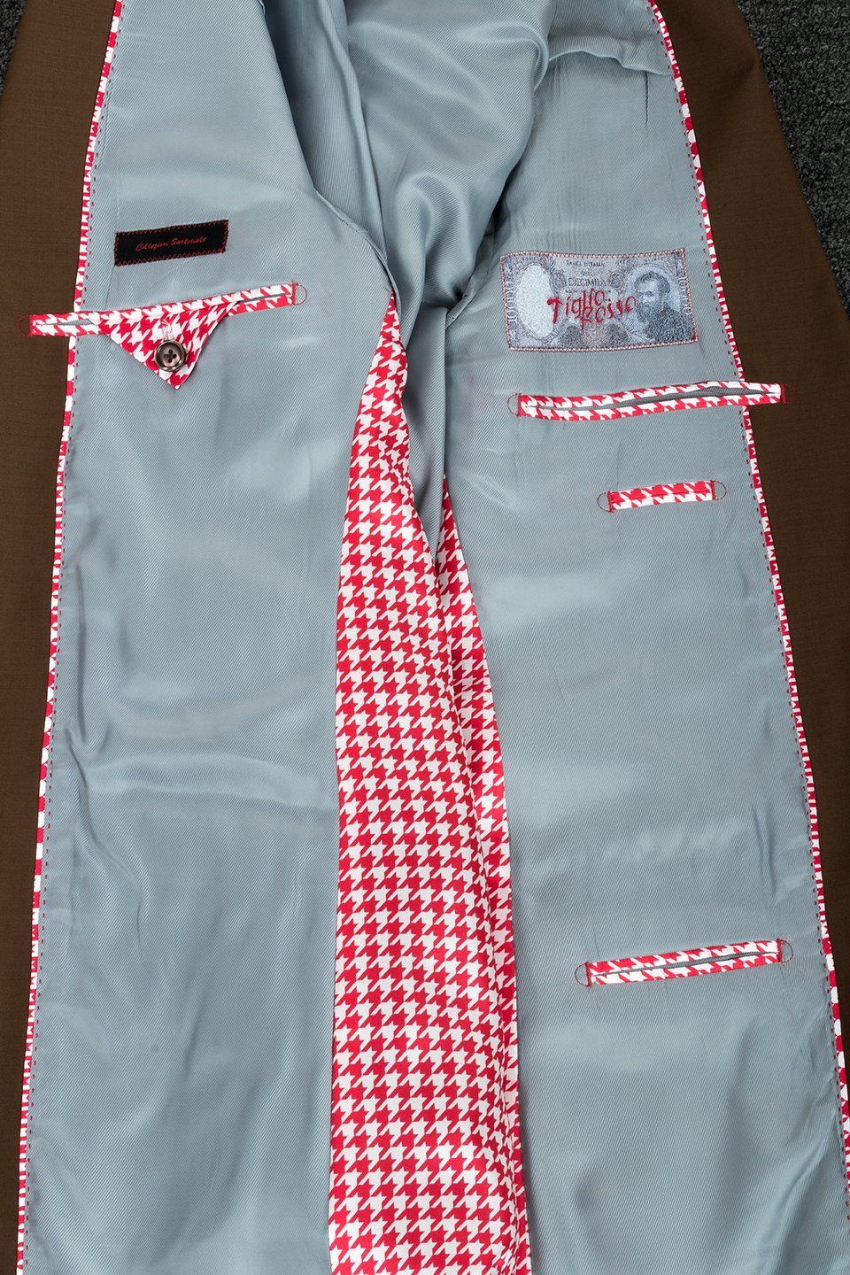 The mannequin showcases a Tiglio Rosso San Giovesse Tobacco three-piece suit, crafted from 100% wool, paired with a blue patterned tie and a floral pocket square.