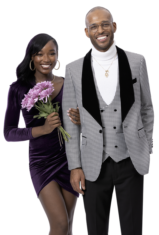 A smiling couple stands together. The woman, in a purple dress, holds pink flowers. The man exudes fashion flair in glasses and the EJ Samuel Blk/White Suit M2782, paired with a white turtleneck.