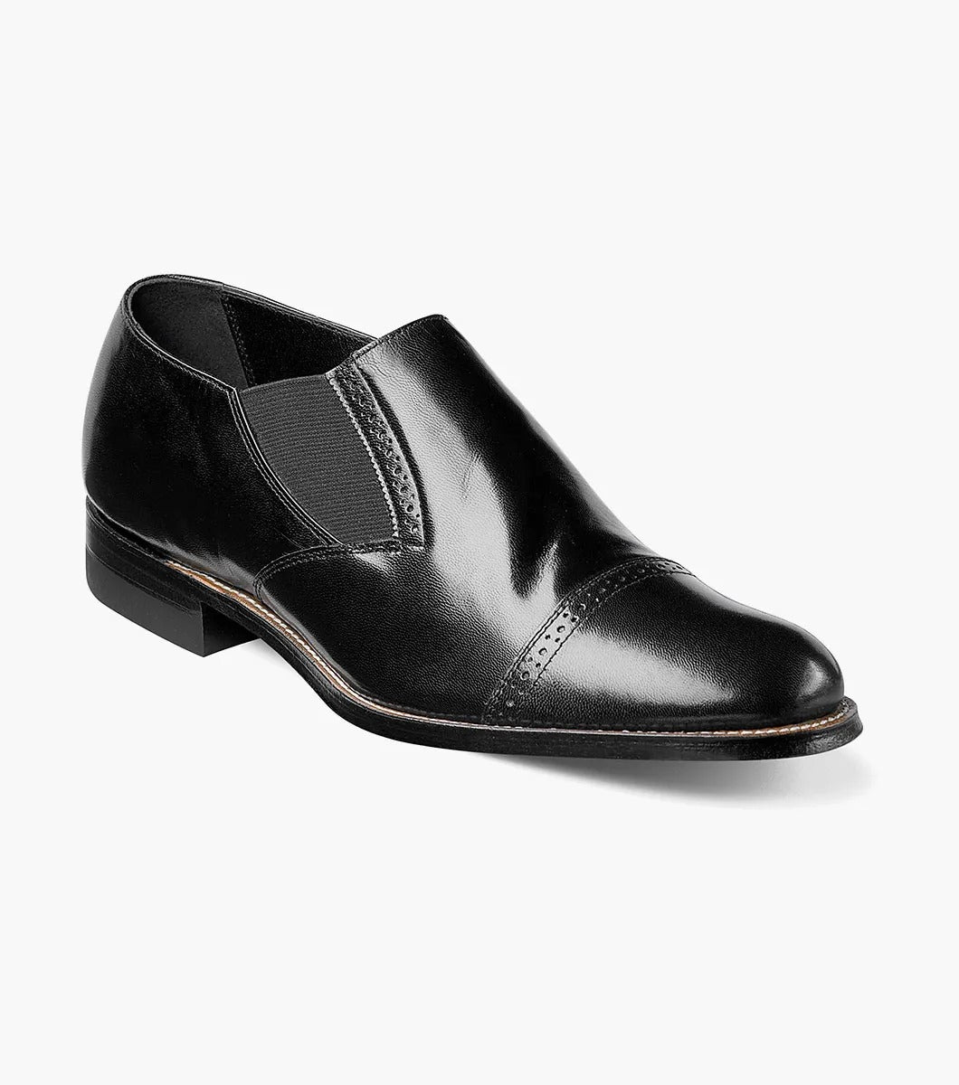 The Stacy Adams MADISON Cap Toe Slip On in black, designated as style number 00017-01, features a sophisticated cap-toe design with elastic side panels, complemented by a leather sole and sleek low heel.