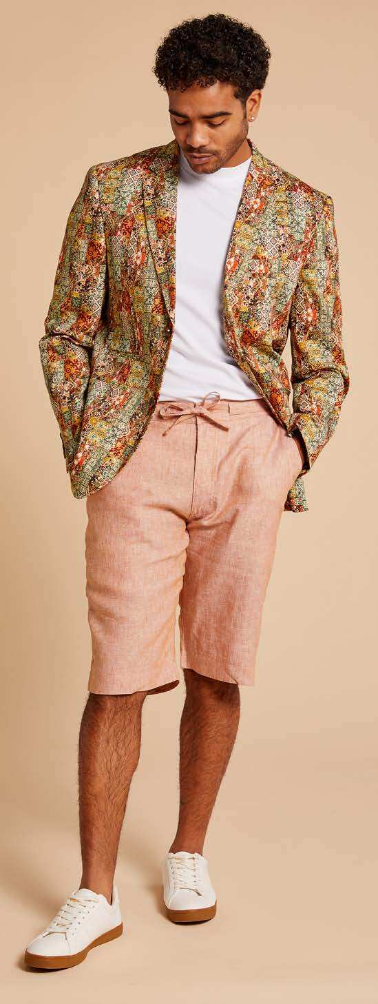 A man wearing the Inserch Patchwork Print Blazer BL261-35 Rust, featuring a colorful digital abstract design and modern fit, adjusts his cotton stretch jacket over a white shirt and pink pants.