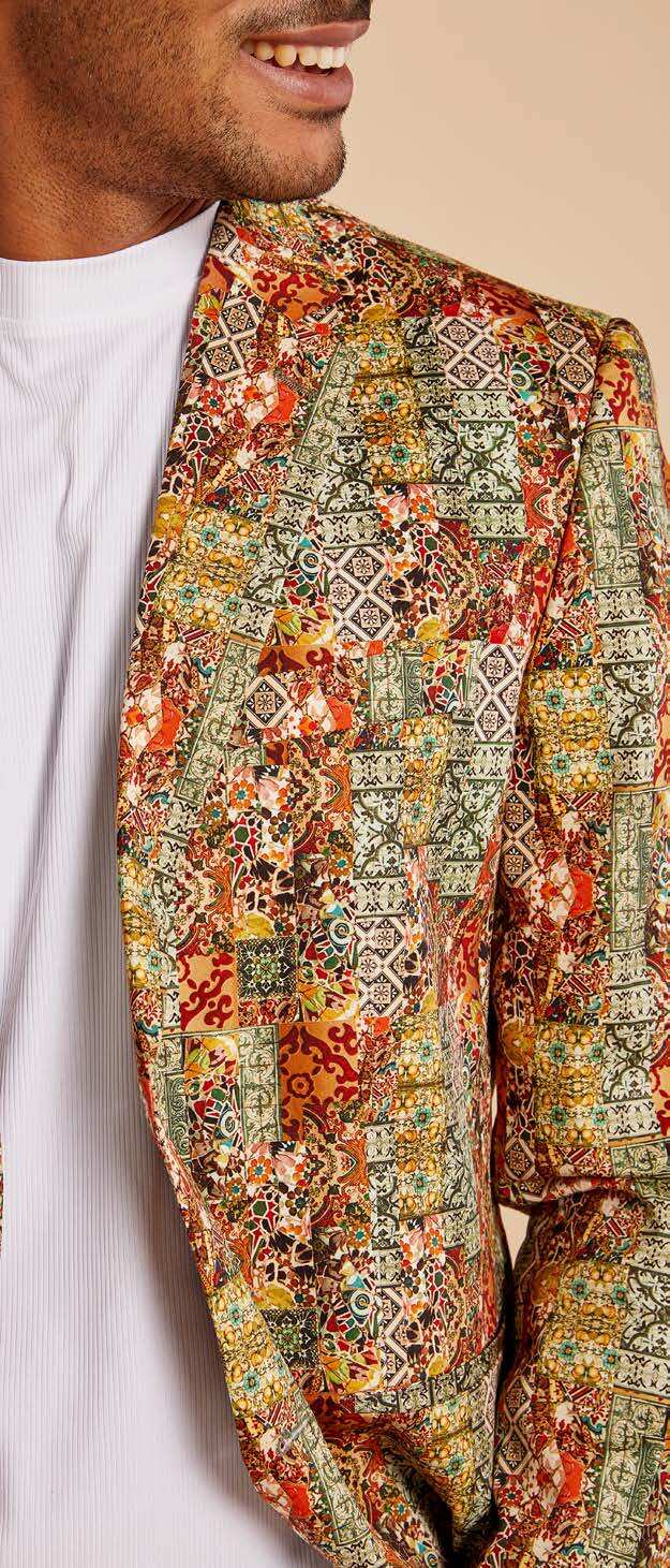A man wearing the Inserch Patchwork Print Blazer BL261-35 Rust, featuring a colorful digital abstract design and modern fit, adjusts his cotton stretch jacket over a white shirt and pink pants.
