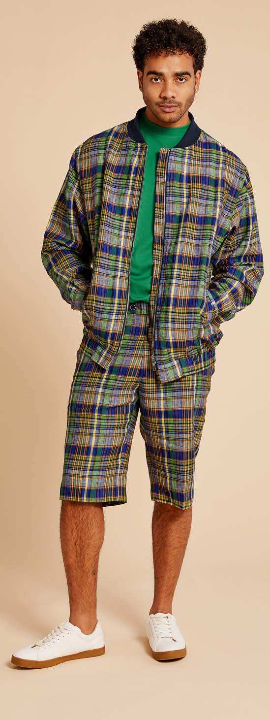 An individual wearing the Inserch Premium Linen Yarn-Dye Madras Plaid Short Zip Jacket in a multi-color pattern over a green shirt is standing against a beige background.