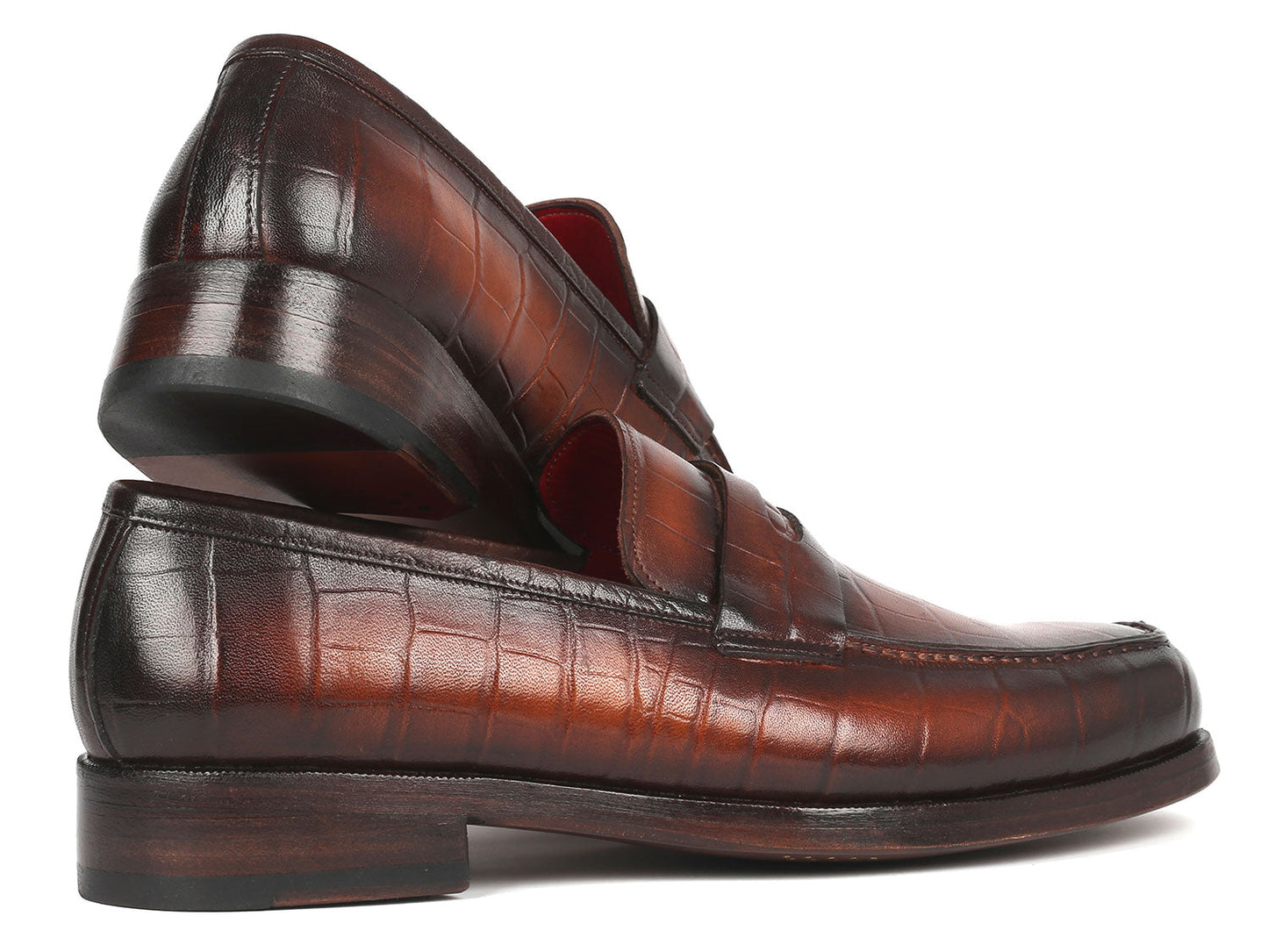 The Paul Parkman Brown Crocodile Embossed Calfskin Penny Loafers - 3857-BRW, featuring a stylish red interior lining, are elegantly displayed with one shoe resting at an angle on the other.