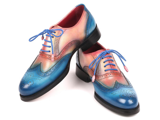 A pair of Paul Parkman Blue & Pink Wingtip Oxfords, model 027-BLUPNK, featuring intricate perforations and blue laces, is elegantly displayed with one shoe atop the other against a white background. These handmade Paul Parkman shoes boast Goodyear welted construction, ensuring both style and durability.
