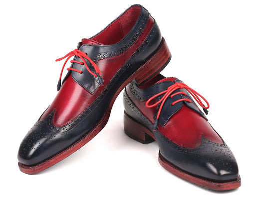 The Paul Parkman Goodyear Welted Wingtip Derby Shoes in Navy & Bordeaux - 511N85 feature a striking two-tone design with hand-painted calfskin leather in red and dark blue, accentuated by intricate brogue detailing and vibrant red laces. These shoes elegantly stand out against the white background with their expertly crafted Goodyear welted wooden sole.