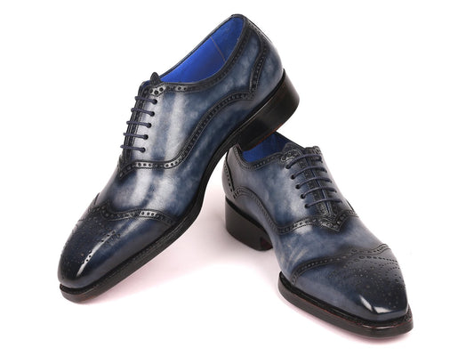 A pair of Paul Parkman Goodyear Welted Oxford Shoes in navy, featuring hand-painted leather with brogue detailing and laces, is displayed with one shoe upright and the other tilted to highlight their made-to-order craftsmanship.