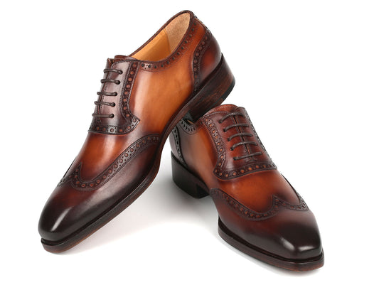 A pair of Paul Parkman Goodyear Welted Wingtip Oxfords in brown, style number 6819-BRW, showcases the elegance of handcrafted leather shoes with decorative perforations. One shoe is positioned on its heel while the other leans gracefully against it, embodying classic sophistication.