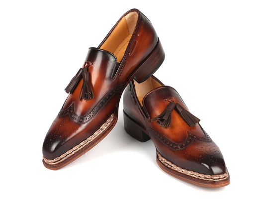 The Paul Parkman Norwegian Welted Tassel Loafers in Brown Burnished - 8507-BRW, crafted with intricate stitching and brogue details, are elegantly displayed with one shoe leaning against the other.