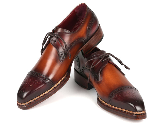 Paul Parkman Norwegian Welted Cap Toe Derby Shoes in Bordeaux and Brown are crafted from rich brown leather with laces, featuring dark brown detailing on the toe and heel. These shoes are stylishly displayed, with one leaning against the other, showcasing their hand-painted elegance.