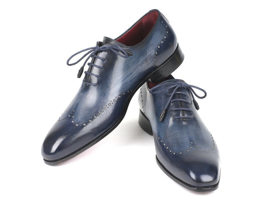 A pair of Paul Parkman Navy Burnished Wingtip Oxfords - 84NT56, showcasing hand-painted leather and intricate detailing, with one oxford style shoe leaning against the other.