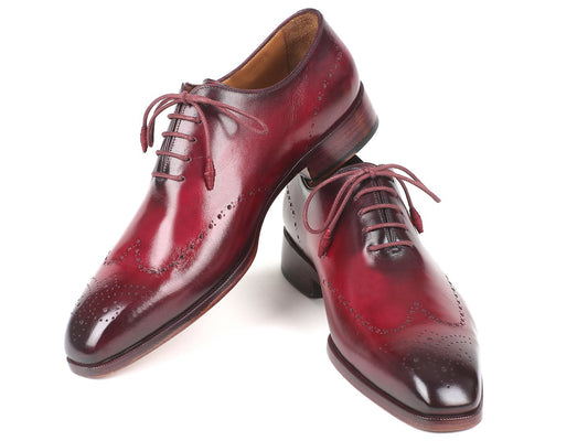 Paul Parkman Bordeaux Burnished Wingtip Oxfords - 84RT83, featuring brogue detailing and hand-painted leather, are showcased with one upright and the other on its side against a white background.