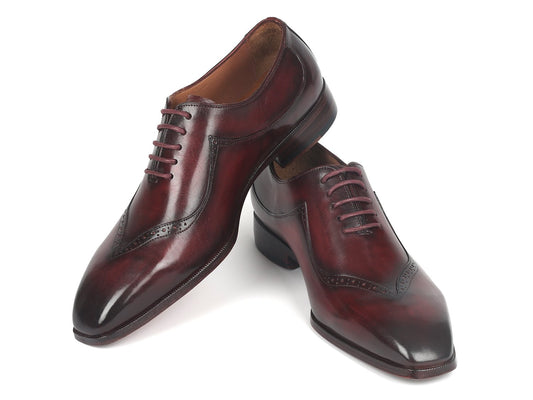A pair of Paul Parkman Dark Bordeaux Hand-Painted Oxfords - 35BRD25, featuring elegant decorative brogue details, with one shoe slightly leaning against the other to highlight their exquisite craftsmanship.