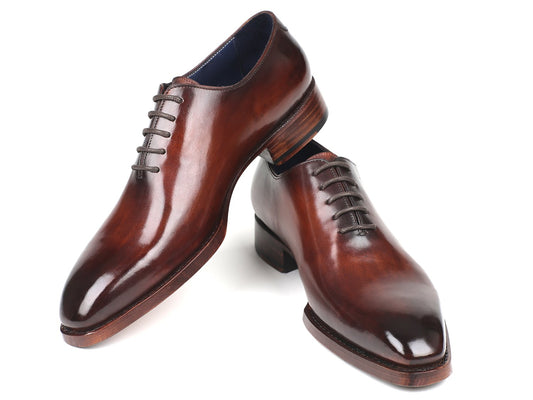 A pair of Paul Parkman Goodyear Welted Wholecut Oxfords in brown, hand-painted leather with laces, one shoe elegantly resting on its side against the other.