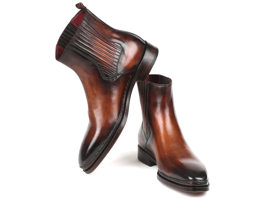 The Paul Parkman Chelsea Boots in Brown Burnished Leather (BT57-BRW) are expertly handmade with calfskin and feature elastic side panels along with low heels. One boot stands upright while the other is tilted slightly, showcasing their polished design.