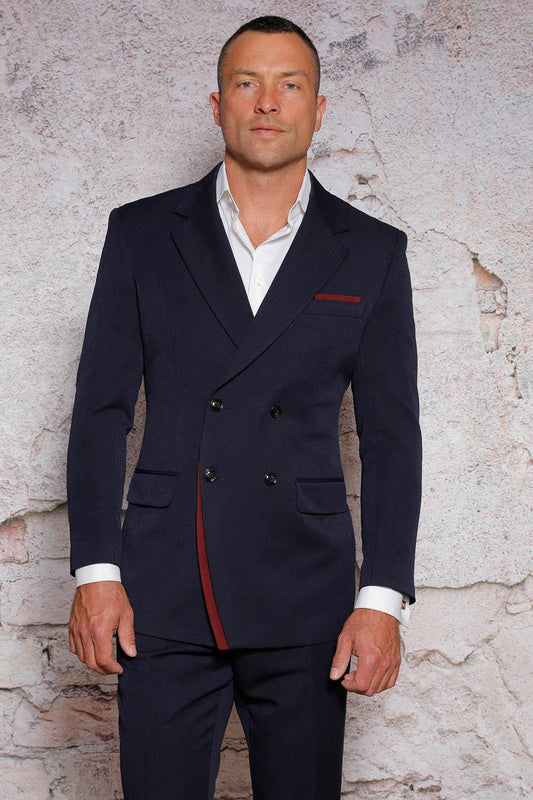A man in a dark, double-breasted Manzini suit from the MANZINI Fancy Double Breasted Red Label collection is standing against a textured, light-colored wall.