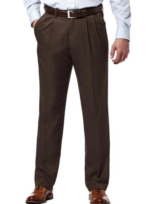 A man wearing Vinci Suits' OP-900 Regular Leg Pleated Pre-Hemmed With Cuffs Dress Pants in brown, paired with a white shirt and brown belt, stands confidently against a plain background with hands in pockets. These pants are stylishly wrinkle-resistant.
