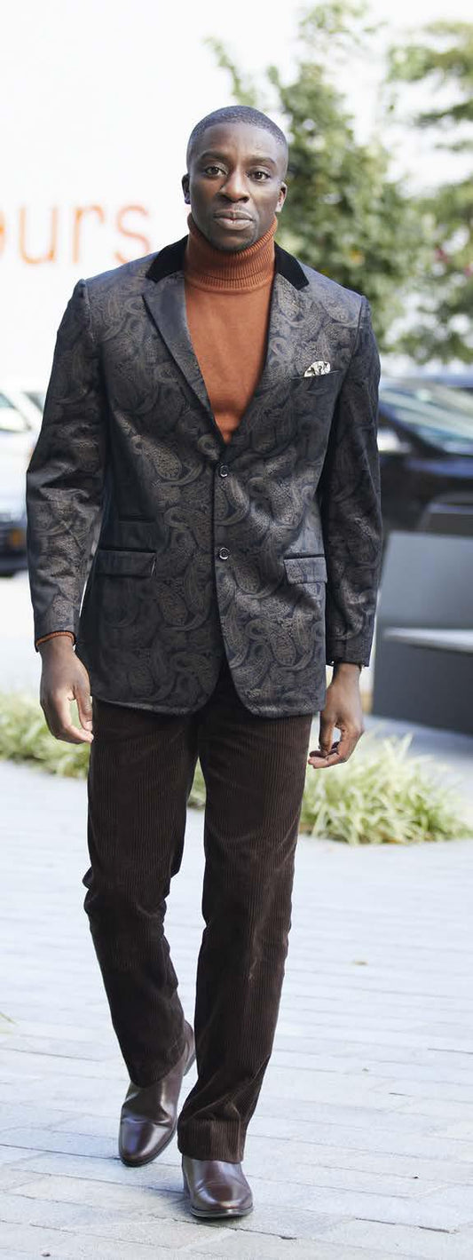 A person walks outdoors in a patterned blazer and brown turtleneck, wearing Inserch's Chocolate Cotton Flat Front Corduroy Pants (P3103-24), with their hands by their sides.