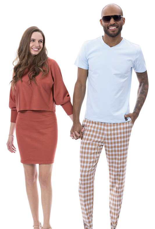 A woman in a red outfit and a man in sunglasses, wearing a modern-fit light blue shirt paired with EJ Samuel Beige Plaid Pants PL146, are holding hands and smiling.