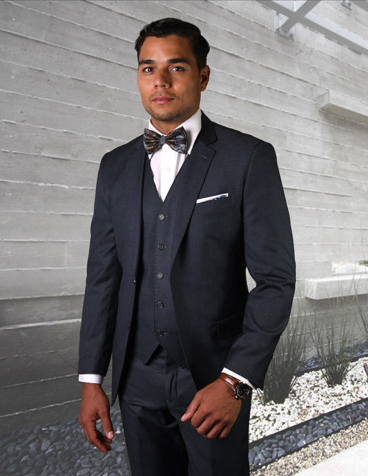 A man wearing the impeccably tailored STATEMENT CLOTHING | STZV-101-H.CHARCL by Statement Clothing, featuring a sleek fit with flat front pants, stands in front of a modern concrete wall background.