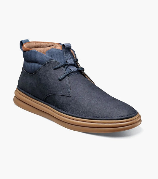 The Stacy Adams Delson Plain Toe Chukka Boot in navy features a leather upper, tan lining, dark laces, and a light brown rubber sole with arch support, shown at an angle to display the side and front.